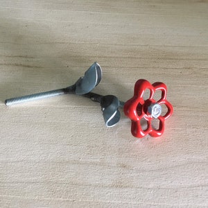 May include: A red metal flower made from a repurposed water valve handle with two silver metal leaves attached to a silver metal stem.
