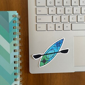 May include: A blue and green kayak sticker with a black paddle on a silver laptop computer.