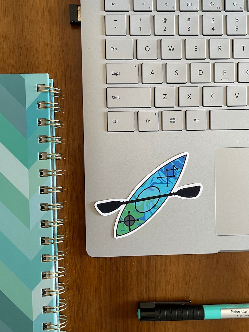 May include: A blue and green kayak sticker with a black paddle on a silver laptop computer.