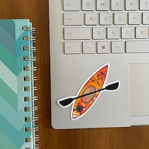May include: A sticker of an orange and yellow kayak with a black paddle on a silver laptop.