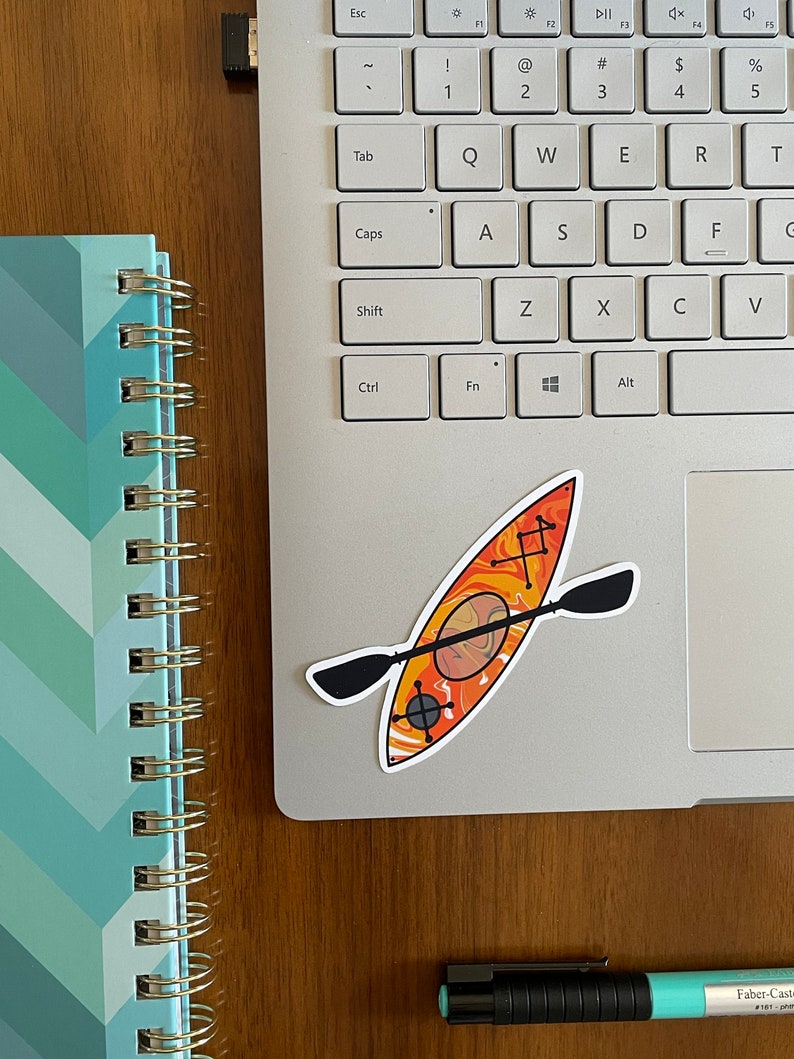 May include: A sticker of an orange and yellow kayak with a black paddle on a silver laptop.
