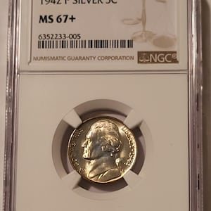 May include: A 1942 P Silver 5C coin, graded MS 67+, encased in a protective holder by Numismatic Guaranty Corporation (NGC). The coin features a profile of a man on the obverse. The holder has the text "1942 P SILVER 5C" and "MS 67+".