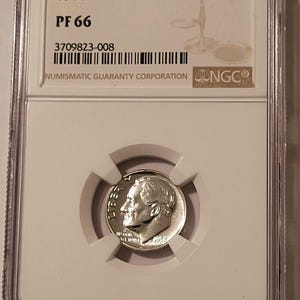 May include: A 1955 10C coin, graded PF 66, encased in a clear protective holder. The coin features a profile of a man and the inscription "LIBERTY". The holder includes a barcode and the "NGC" logo.