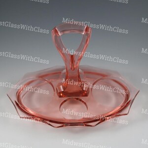 May include: A pink glass serving tray with a handle. The tray has a hexagonal shape with three circular indentations and a central handle. The glass has a smooth, glossy finish. The text "MidwstGlassWithClass" is repeated across the image.