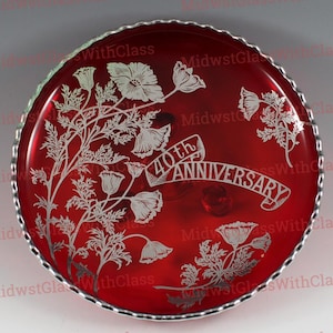 May include: A round, red glass plate with a silver rim. The plate features an etched floral design and the words "40th Anniversary" in a banner. The plate is a decorative item.