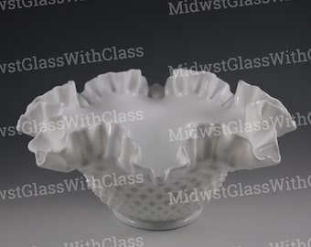 May include: A white hobnail glass bowl with a ruffled rim. The bowl has a wide, open design with a textured hobnail pattern on the lower portion. The ruffled edge adds a decorative touch to this vintage glassware.