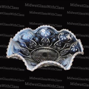 May include: A decorative, ruffled-edge glass bowl with a blue and white opalescent design. The bowl features a floral pattern and a textured center. The background is black with the text "MidwstGlassWithClass" repeated.