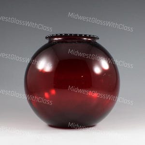 May include: A round, ruby red glass vase with a slightly textured rim. The vase has a spherical shape and a glossy finish, reflecting light. The text "MidwestGlassWithClass" is repeated around the image.