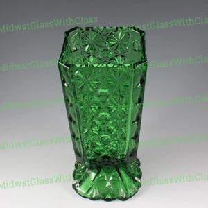 May include: A green glass vase with a geometric pattern. The vase has a faceted design with starburst and diamond shapes. The base is also faceted, and the vase is approximately 8 inches tall.