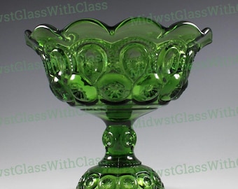 May include: A green glass pedestal bowl with a scalloped rim and star and moon pattern. The bowl sits on a round base and a decorative stem. The words "MidwestGlassWithClass" are watermarked on the image.