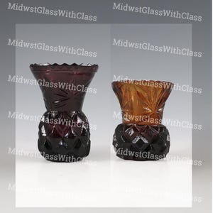 May include: Two decorative glass vases. One is a deep purple color, and the other is a golden amber color. Both vases have a diamond-patterned base and a textured, flared top. The text "MidwestGlassWithClass" is repeated across the image.