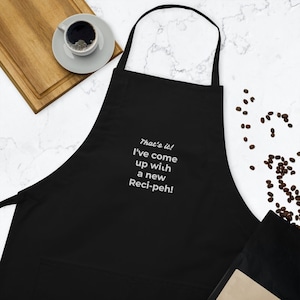 Puede incluir: Delantal de cocina negro con un dicho bordado en blanco: "That's it! I've come up with a new Reci-peh!"