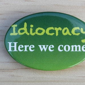 May include: A green and yellow button with the text "Idiocracy Here we come!" printed on it.