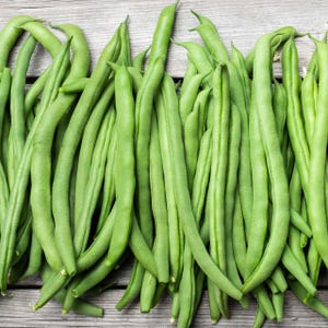 May include: A bunch of fresh green string beans, arranged in a row on a wooden surface.