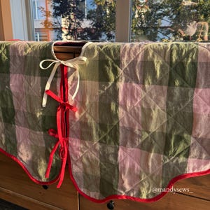 May include: A quilted tree skirt with a green and pink plaid pattern. The skirt has a red trim and is tied with white and red ribbons. The text "@mandysews_" is visible on the bottom right.