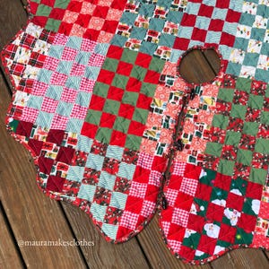 May include: A handmade Christmas tree skirt with a patchwork design. The skirt features red, green, and white fabrics with various patterns, including checks, stripes, and gift box motifs. The skirt has a scalloped edge and a center opening.