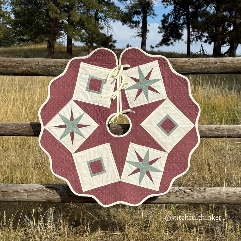 May include: A quilted Christmas tree skirt with a scalloped edge. The skirt features a burgundy background with cream-colored squares and teal star designs. A cream-colored tie is at the top. The skirt is approximately 48 inches in diameter.