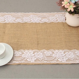 May include: A burlap table runner with white lace trim. The runner has a rustic look and would be perfect for a wedding or other special occasion.