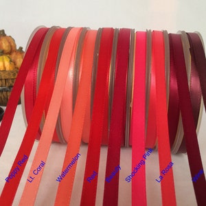 Könnte beinhalten: Eine Sammlung von 10 Spulen Satinband in verschiedenen Rot-, Rosa- und Koralltönen. Die Bandfarben sind mit ihren Namen beschriftet: Rubin, Mohnrot, Hellkoralle, Wassermelone, Rot, Burgunder, Schockrosa, La Rosa, Wein und Roséwein.