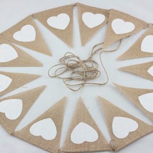 May include: A burlap banner with white heart-shaped cutouts. The banner is strung together with twine and is ready to be hung.