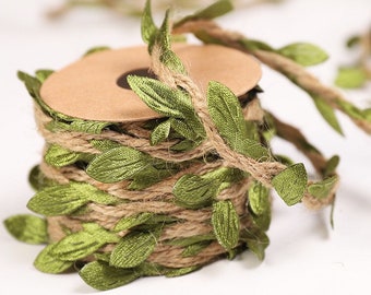 Puede incluir: Un rollo de cuerda con hojas de tela verde unidas. La cuerda es marrón y las hojas son de color verde oscuro.
