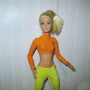 May include: A doll with blonde hair in a ponytail wearing a bright orange crop top and lime green leggings.