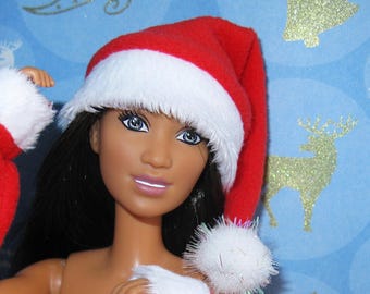 May include: A doll dressed in a red and white Santa outfit, including a hat. The doll has dark hair, blue eyes, and a fair complexion. The background is light blue with gold glitter Christmas decorations.
