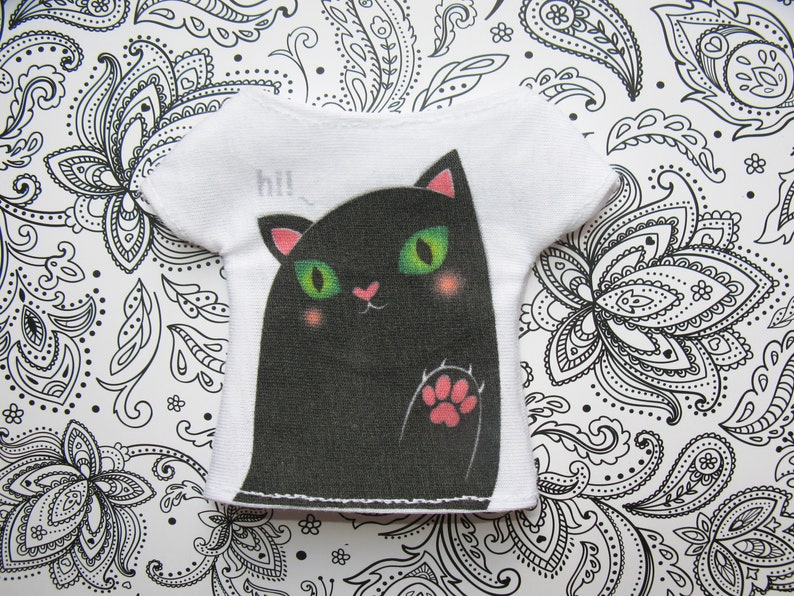 Pode incluir: Camiseta branca com um gr&aacute;fico de um gato preto e a palavra "hi!" impressa na frente.