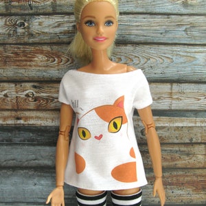 Pode incluir: Camiseta branca com um gr&aacute;fico de gato de desenho animado em laranja e branco. O gato tem um nariz de cora&ccedil;&atilde;o rosa e o texto "hill" est&aacute; acima do gato.