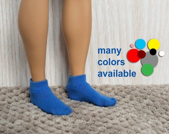 May include: A pair of blue knitted socks. The socks are displayed on a doll's legs, standing on a textured, light brown surface. The text "many colors available" is visible in the image.