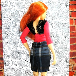 May include: A red and black doll with long red hair wearing a red top with a black lace overlay and a plaid skirt.