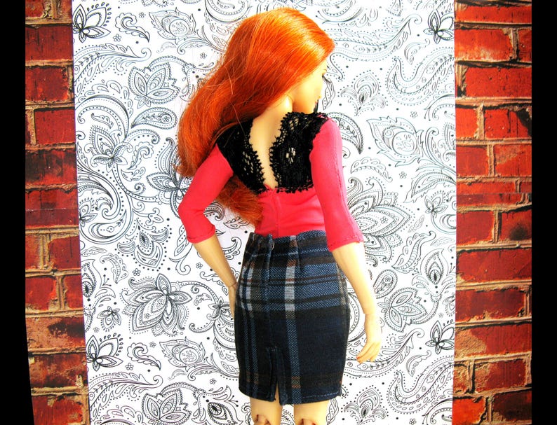 May include: A red and black doll with long red hair wearing a red top with a black lace overlay and a plaid skirt.