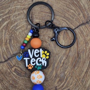 May include: A black keychain with a Vet Tech charm. The charm has a paw print design and the words "Vet Tech" in white. The keychain also features colorful beads and a heart charm.