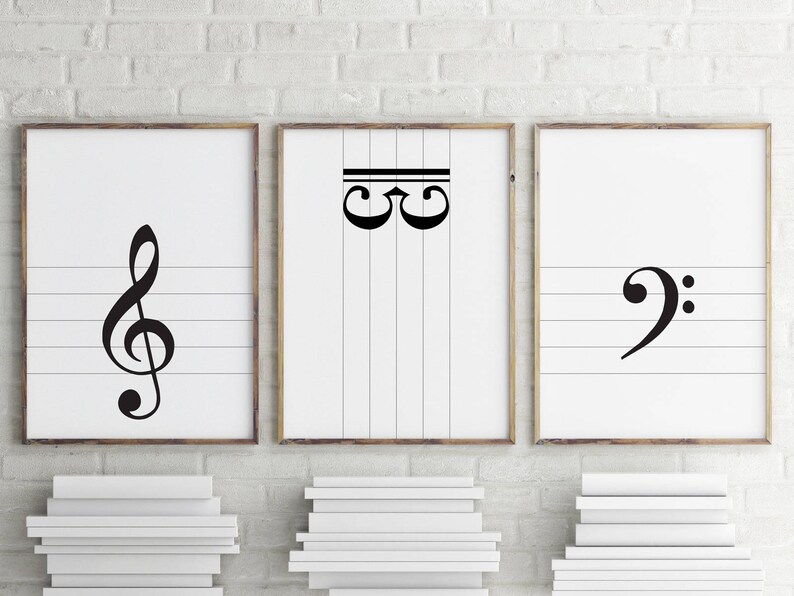 May include: Three framed prints with musical notes on a white brick wall. The left print features a treble clef, the middle print features a staff with two C notes, and the right print features a bass clef.