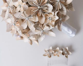 May include: A bouquet of cream-colored paper flowers made from book pages, with white pearl accents. The bouquet is tied with a white satin ribbon. There are two smaller paper flower hair combs, one with cream flowers and one with white flowers.