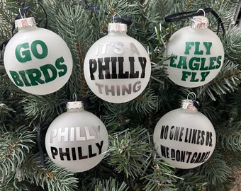 May include: Five white Christmas baubles with black and green lettering. The baubles read "Go Birds", "It's a Philly Thing", "Fly Eagles Fly", "Philly Philly", and "No One Likes Us, We Don't Care".