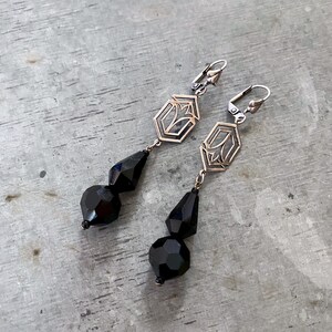 May include: A pair of silver dangle earrings with black faceted glass beads. The earrings feature a geometric design with a hexagonal shape.