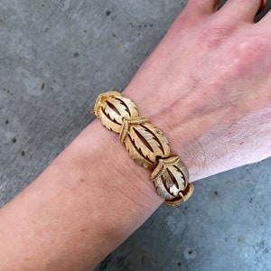 May include: Gold-tone bracelet with a leaf design. The bracelet is made of linked oval-shaped pieces with a textured surface.
