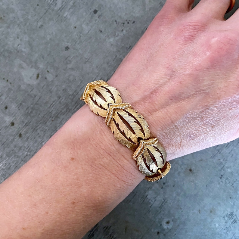 May include: Gold-tone bracelet with a leaf design. The bracelet is made of linked oval-shaped pieces with a textured surface.