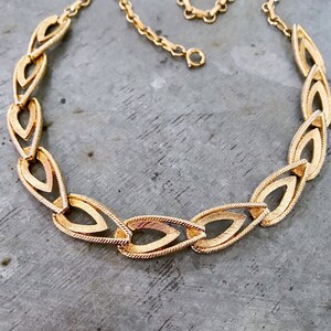 May include: A gold-tone necklace with a chain link design featuring interlocking teardrop-shaped links.