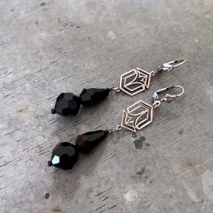 May include: A pair of silver earrings with black faceted glass beads and geometric designs. The earrings have a hook closure.