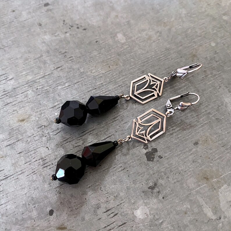 May include: A pair of silver earrings with black faceted glass beads and geometric designs. The earrings have a hook closure.