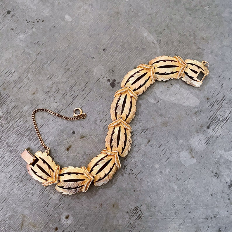 May include: A gold-tone bracelet with a leaf design. The bracelet is made of metal and has a chain link closure.