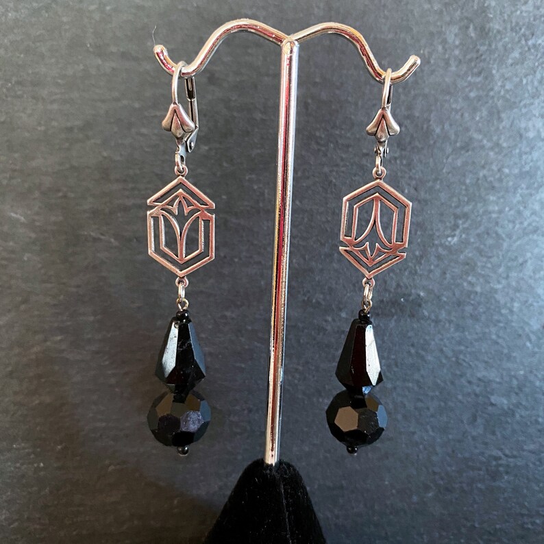 May include: A pair of silver earrings with geometric designs and black teardrop-shaped beads.