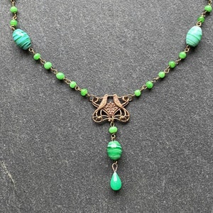 Peut inclure: Un collier de perles de verre vert avec un pendentif en or repr&eacute;sentant deux oiseaux. Le pendentif est attach&eacute; &agrave; une perle de verre verte.