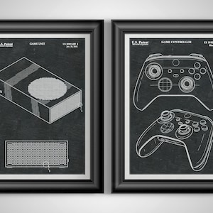 May include: Two framed patent prints featuring gaming technology. One print shows a game unit design, the other a game controller. Both prints are in black frames with white line drawings on a dark background.