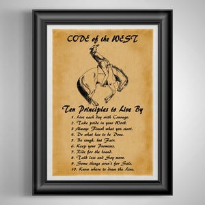 May include: A framed print on a tan background featuring a black ink illustration of a person riding a bucking horse. The text reads CODE of the WEST, Ten Principles to Live By, and lists ten numbered rules starting with Live each day with Courage.