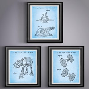 May include: Three framed prints featuring blue and white technical drawings of spacecraft and vehicles. The prints are in black frames and include schematics of a spaceship, an AT-AT walker, and TIE fighters.