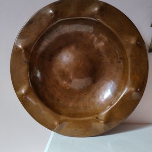 May include: A large, round, copper serving dish with a slightly raised rim and a smooth, shiny surface.