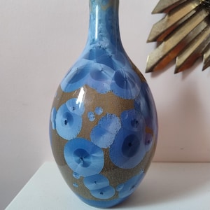 May include: A ceramic vase with a blue and brown crystalline glaze. The vase has a rounded body and a narrow neck. The blue glaze features circular patterns, creating a unique decorative piece. The vase is approximately 25 cm tall.